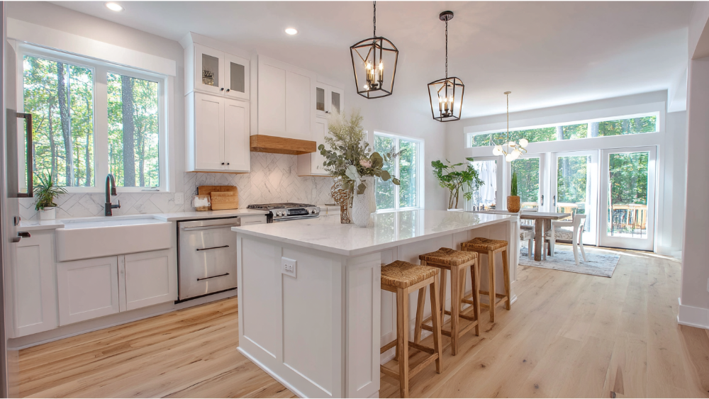 Bright kitchen with white shaker cabinets, light wood flooring, and a large island near a sunlit dining space.