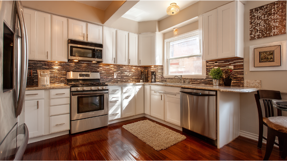 Compact kitchen with white cabinets, stainless steel appliances, and mosaic tile backsplash.