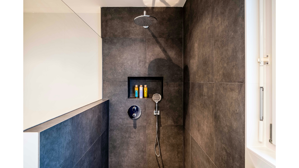 Walk-in shower with dark tile walls and built-in shampoo niche.